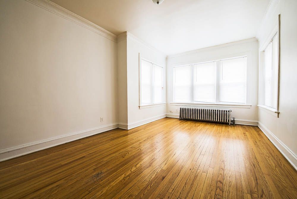 Empty room with hardwood floors, white walls, and a large window.
