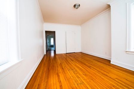 Empty room with hardwood floors, white walls, and a doorway leading to another room.