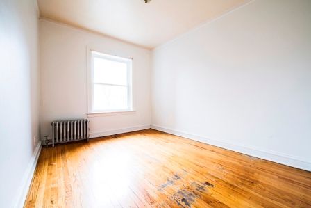 Empty room with hardwood floors, window, radiator, and white walls.