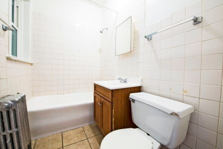Small, tiled bathroom with a tub, toilet, vanity, and radiator.