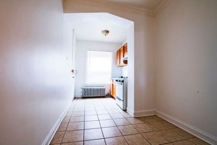 Narrow hallway leading to a small kitchen with tile flooring, a stove, and a window.