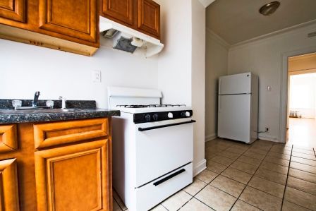 Kitchen with wooden cabinets, white stove and refrigerator, and tiled floor.