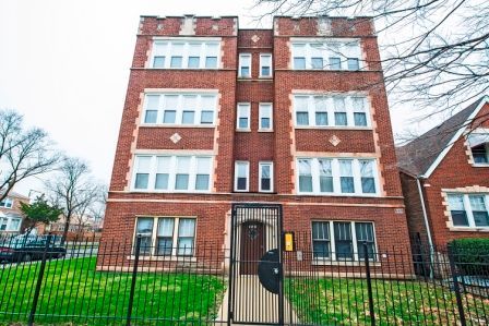 Four-story brick apartment building with black iron gate and green lawn.