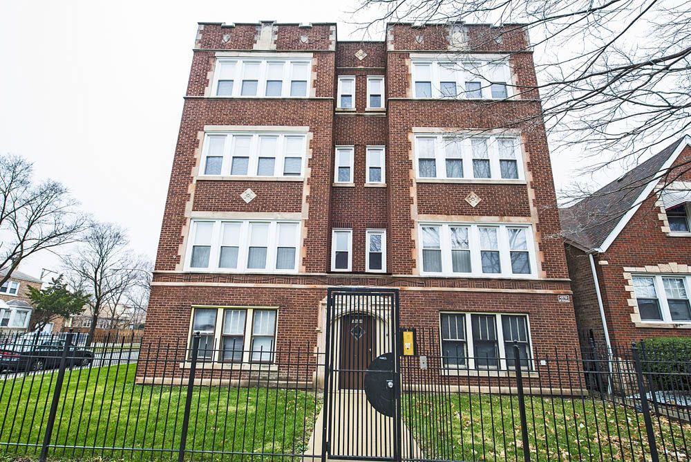 Brick apartment building with decorative accents, black gate and fence, overcast day.
