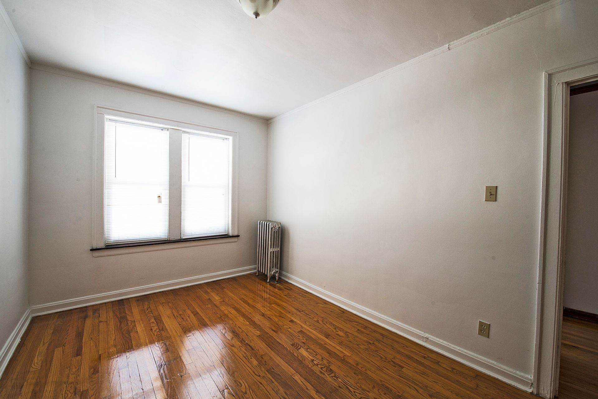 Empty room with hardwood floors, a window, and a radiator. White walls and trim.