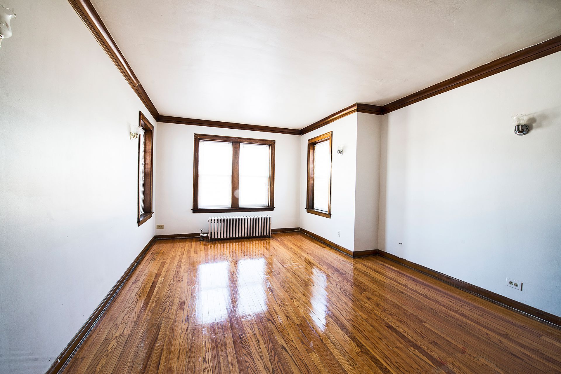 Empty room with hardwood floors, white walls, and wooden trim. Natural light enters through the windows.