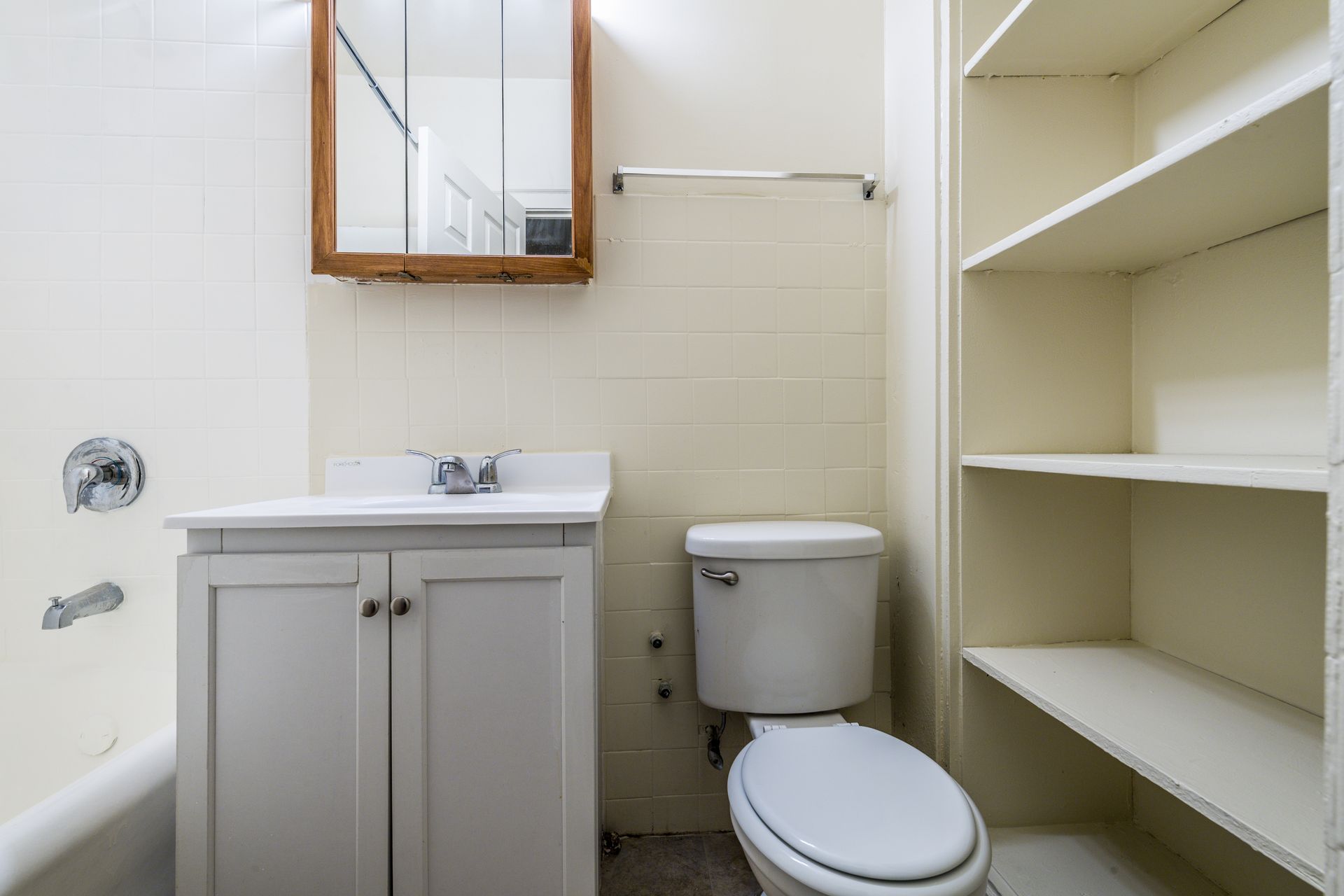 Bathroom with white vanity, toilet, and shelving; a mirror and tub with shower fixtures are also present.