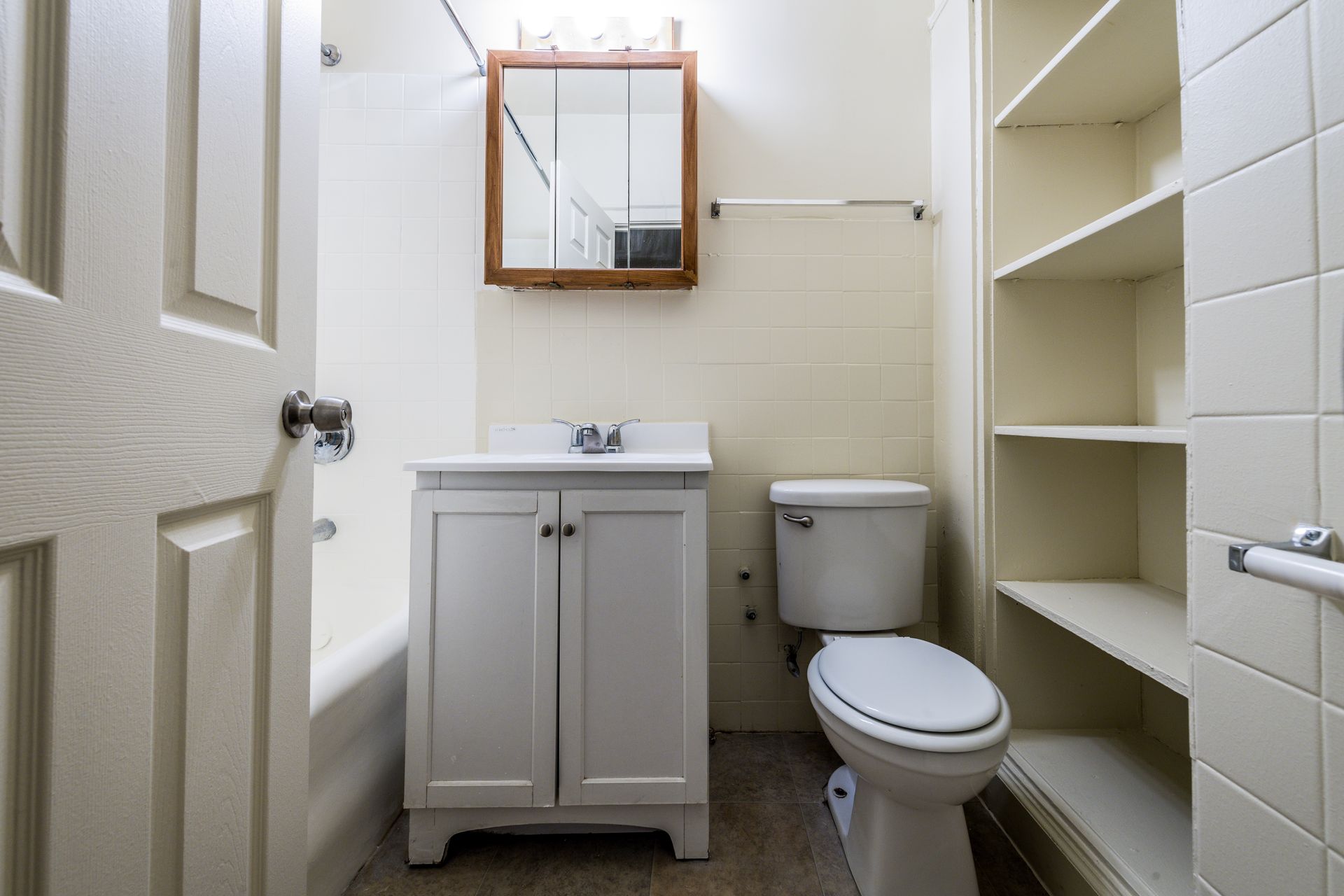 Bathroom with white vanity, toilet, medicine cabinet, and built-in shelving.