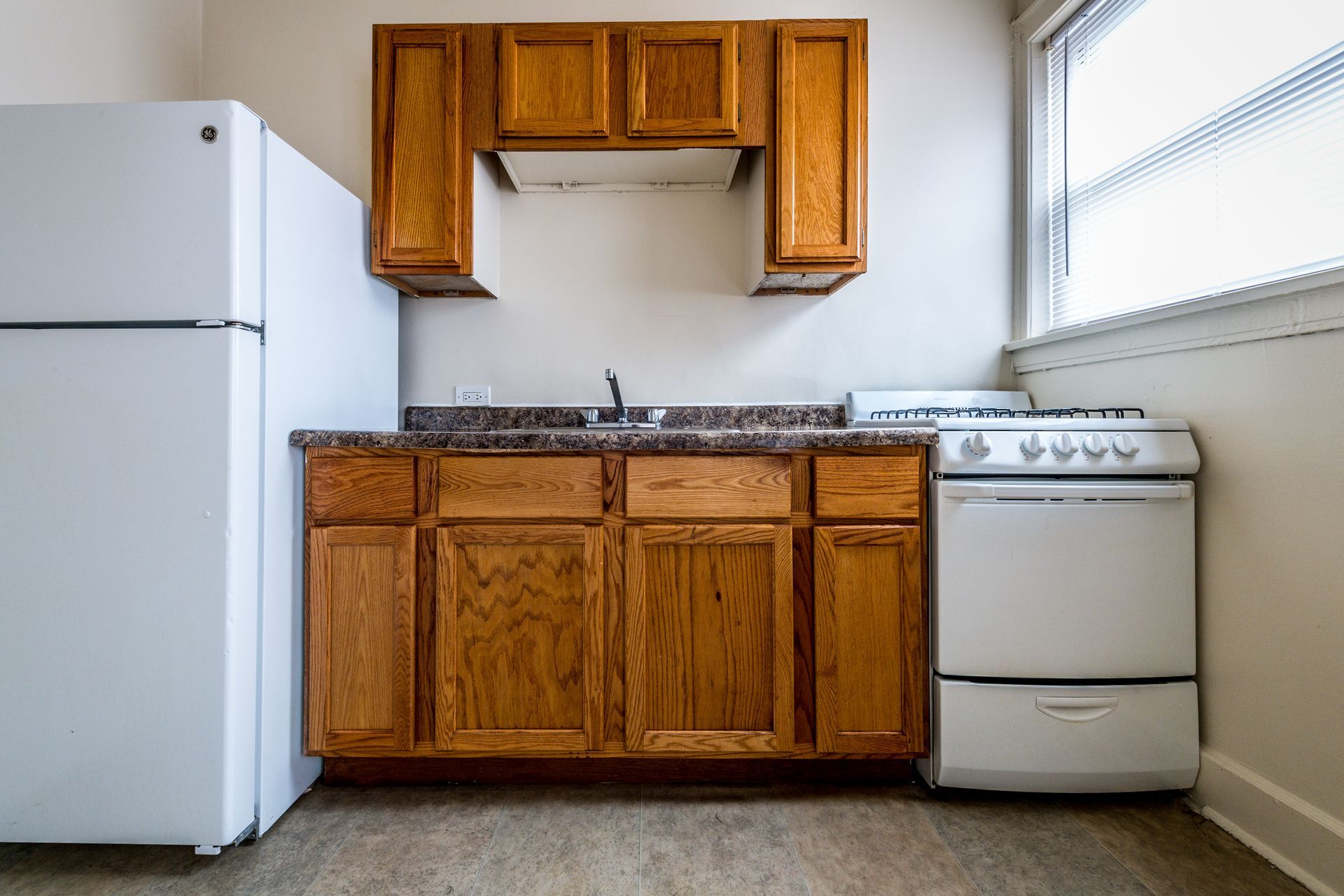 Small kitchen with light brown cabinets, white appliances, and a window.