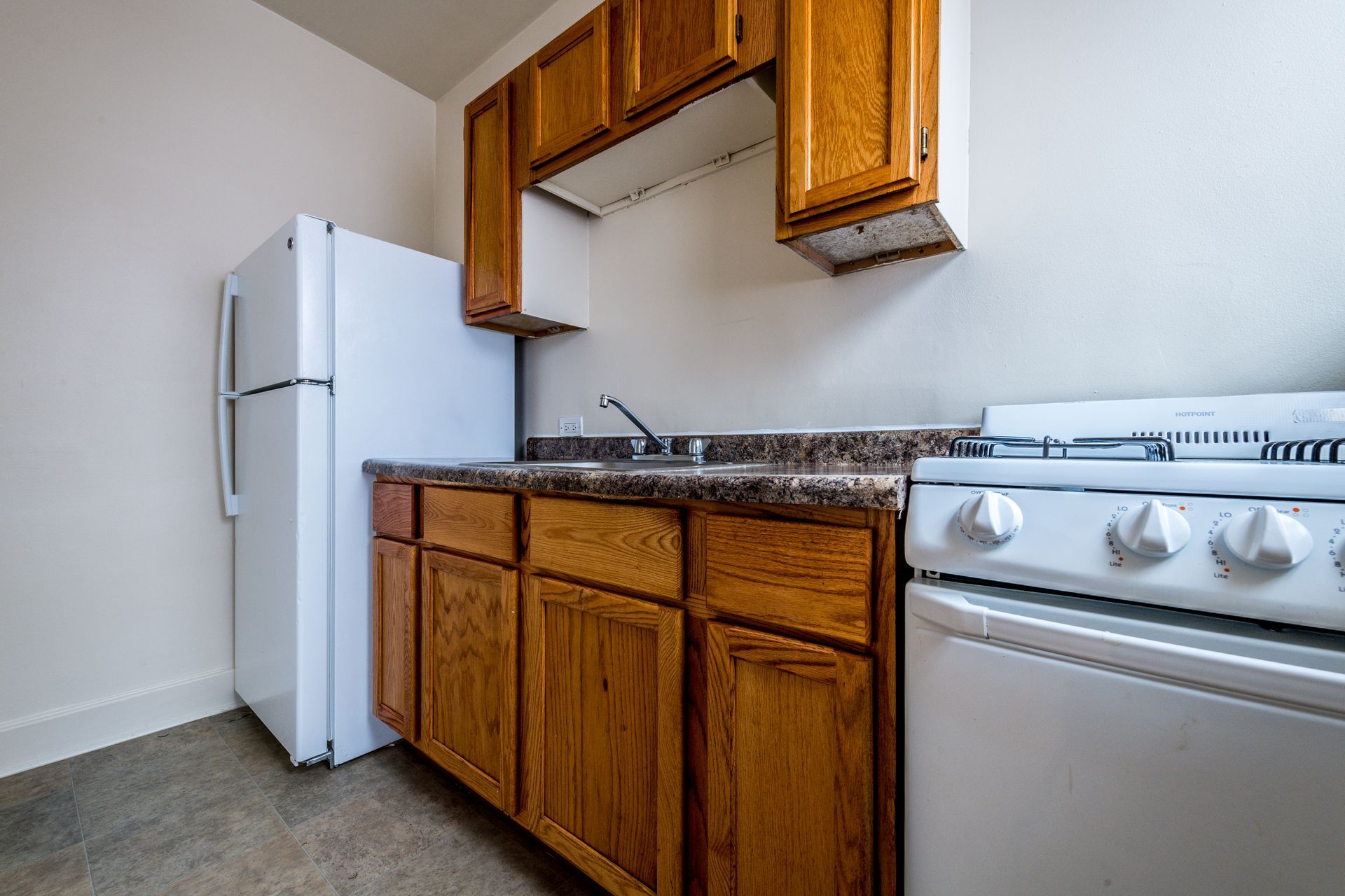 Small kitchen with white refrigerator, stove, wooden cabinets, and a sink.