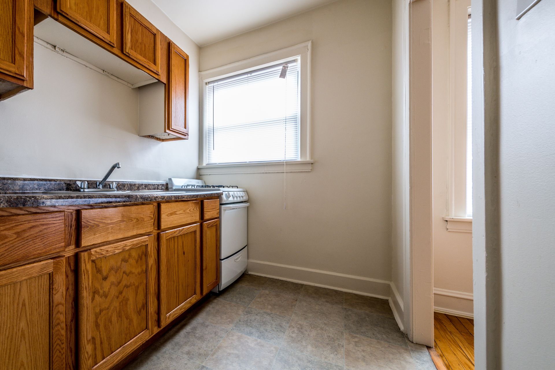 Kitchen with wooden cabinets, a sink, and a washing machine near a window. Light-colored walls and floor.