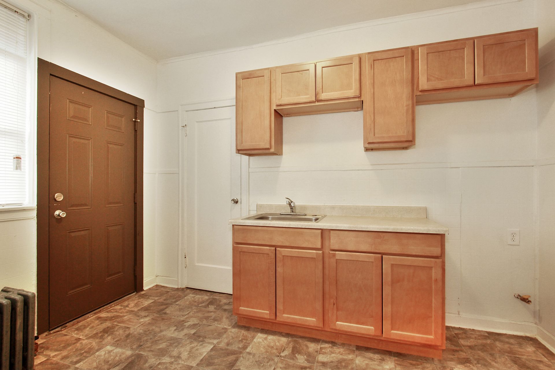 Kitchen with light brown cabinets, sink, and dark brown door.