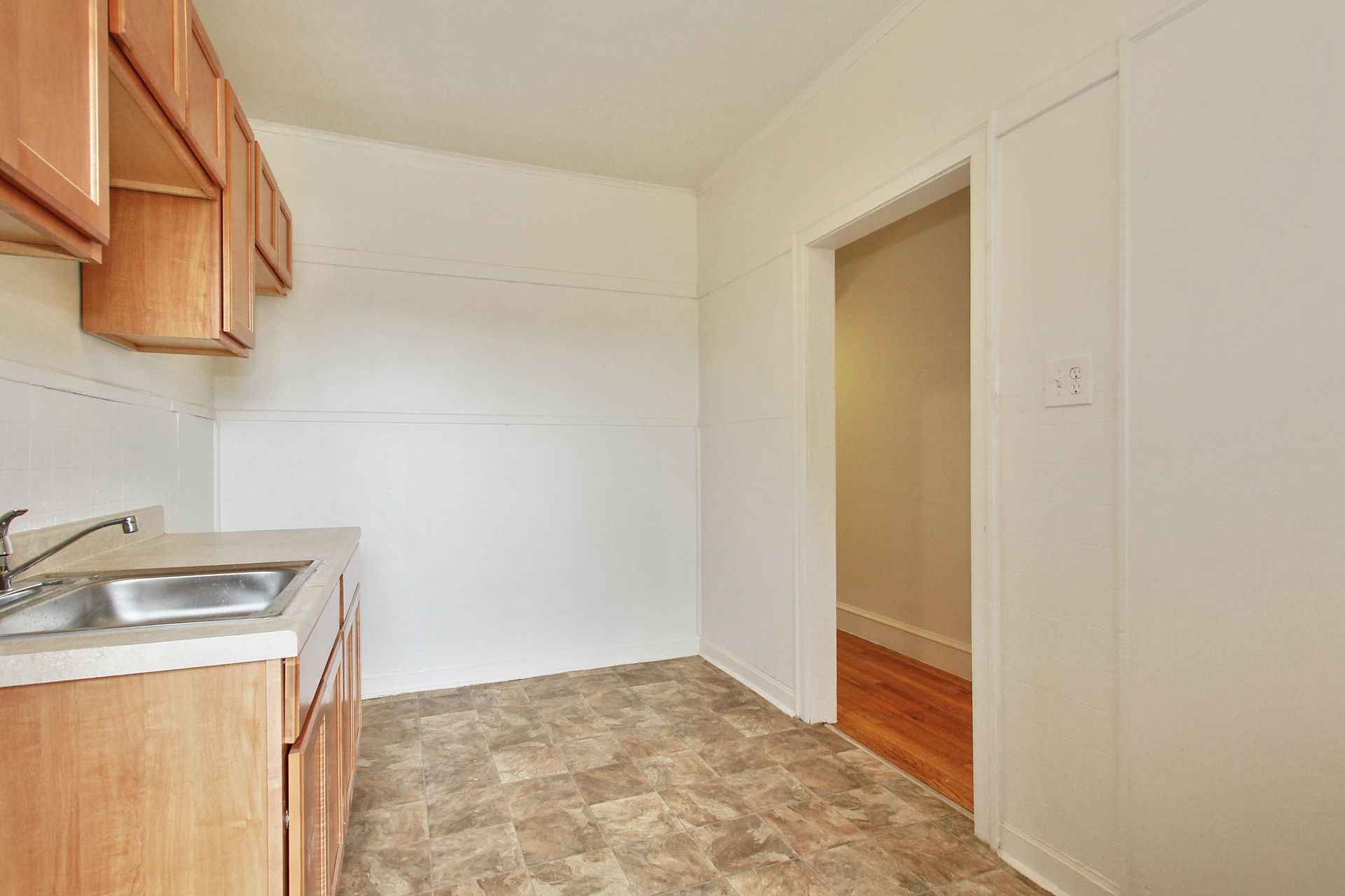 Small kitchen with light cabinets, a sink, and a doorway leading to a room with hardwood floors.