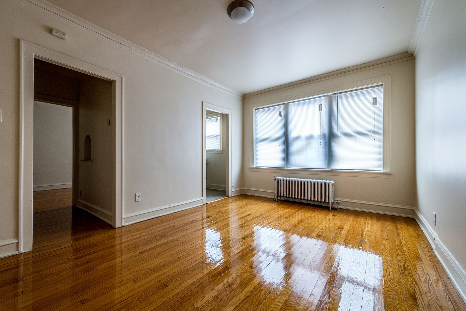 Empty room with wood floors, radiator, and a window with blinds.
