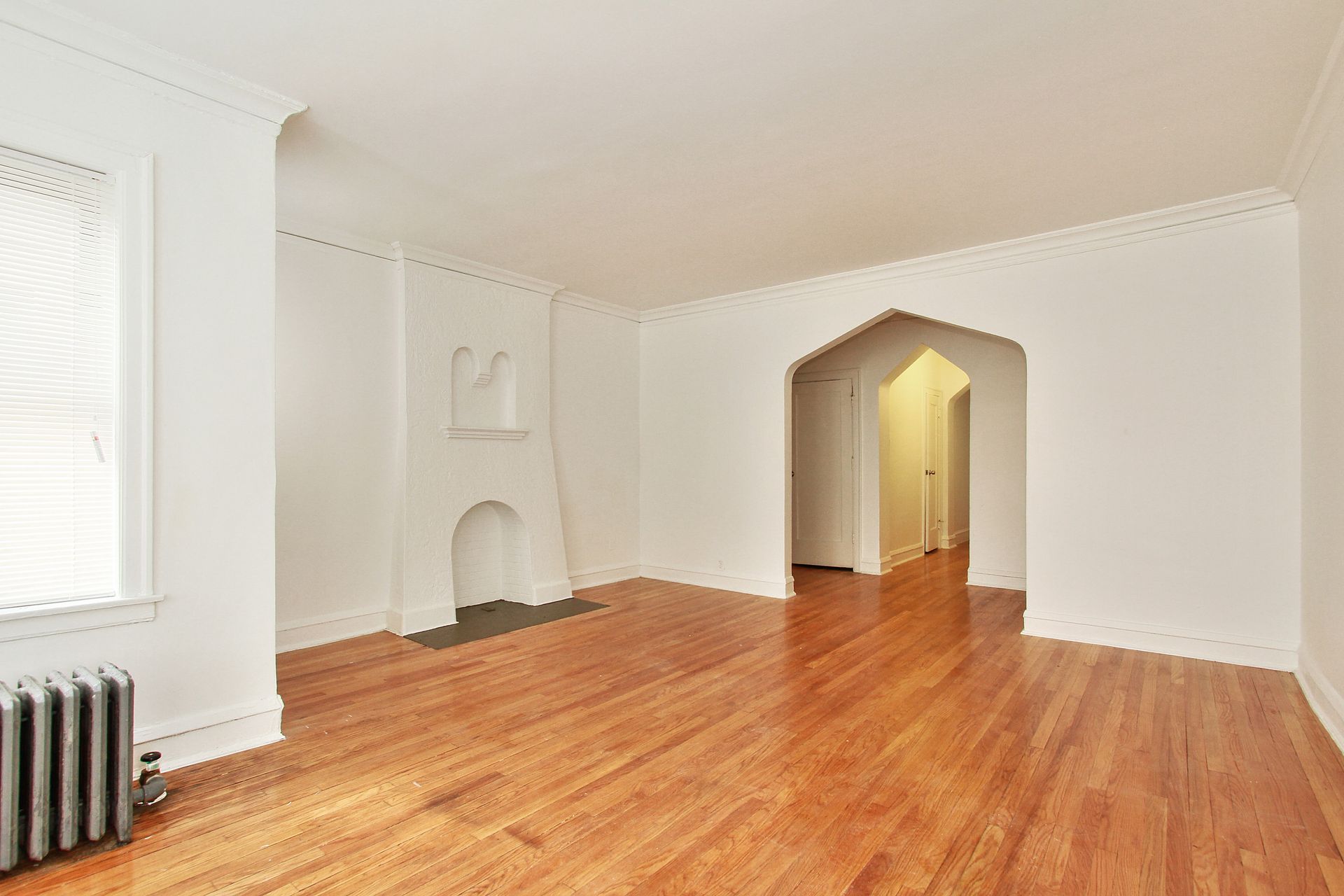 Empty room with hardwood floors, white walls, arched doorway, and a fireplace.