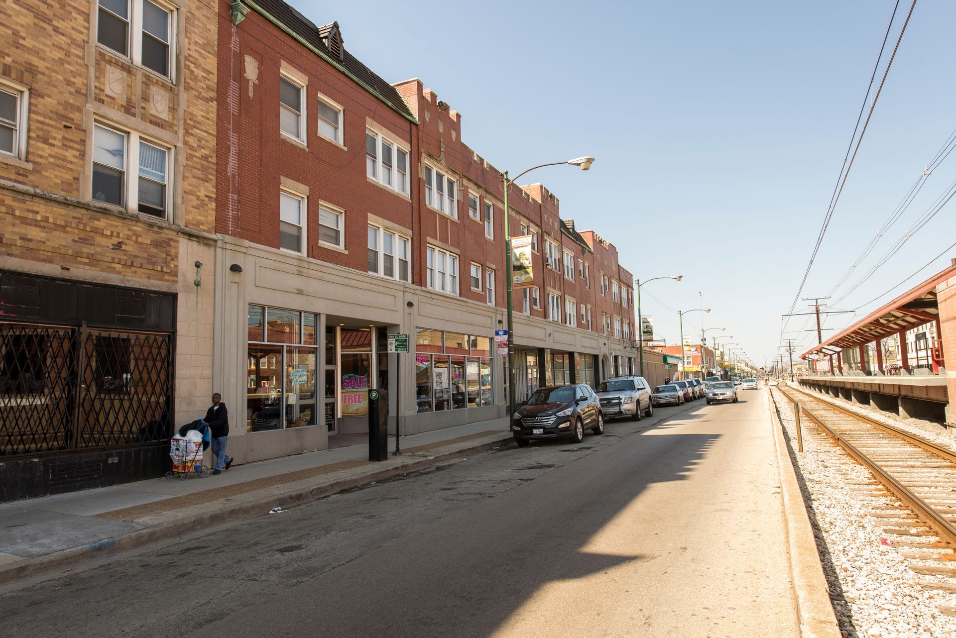 Street scene with brick buildings, parked cars, train tracks, and a clear sky.