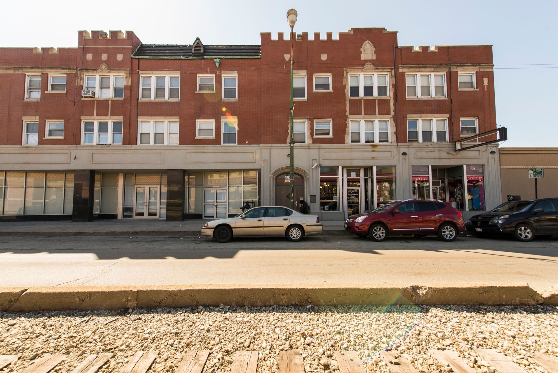 Brick building with storefronts and cars parked on street.