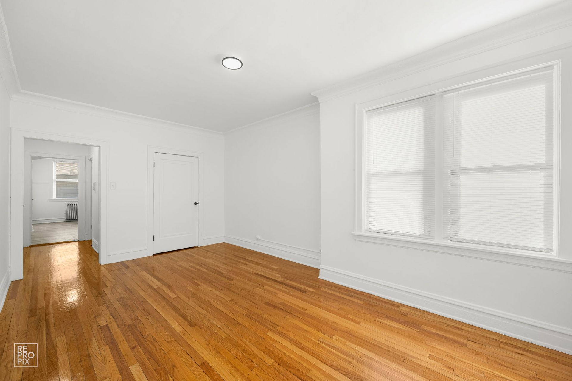 Empty room with hardwood floors, white walls, and a window with blinds.