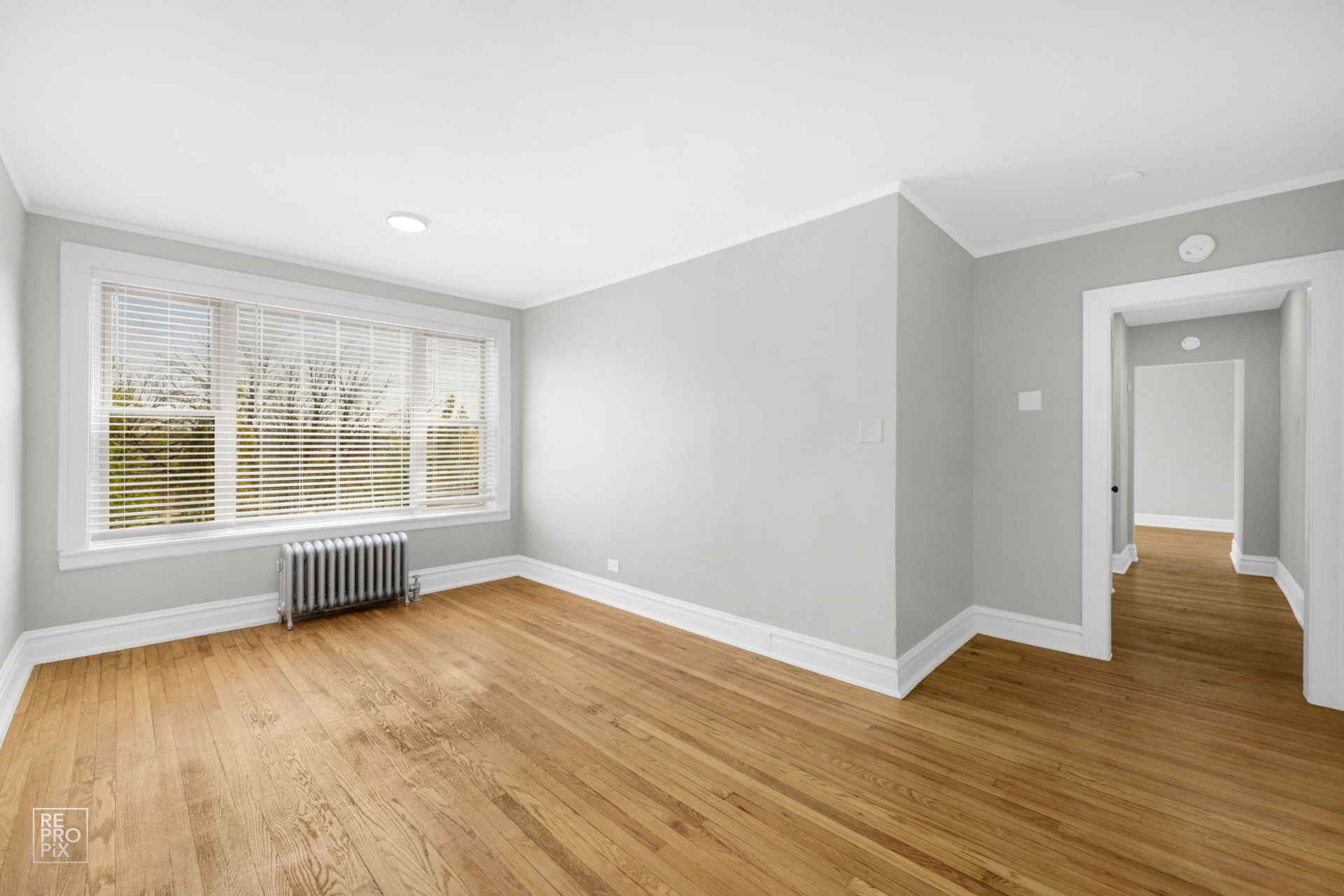 Empty room with hardwood floors, a large window, and light gray walls.
