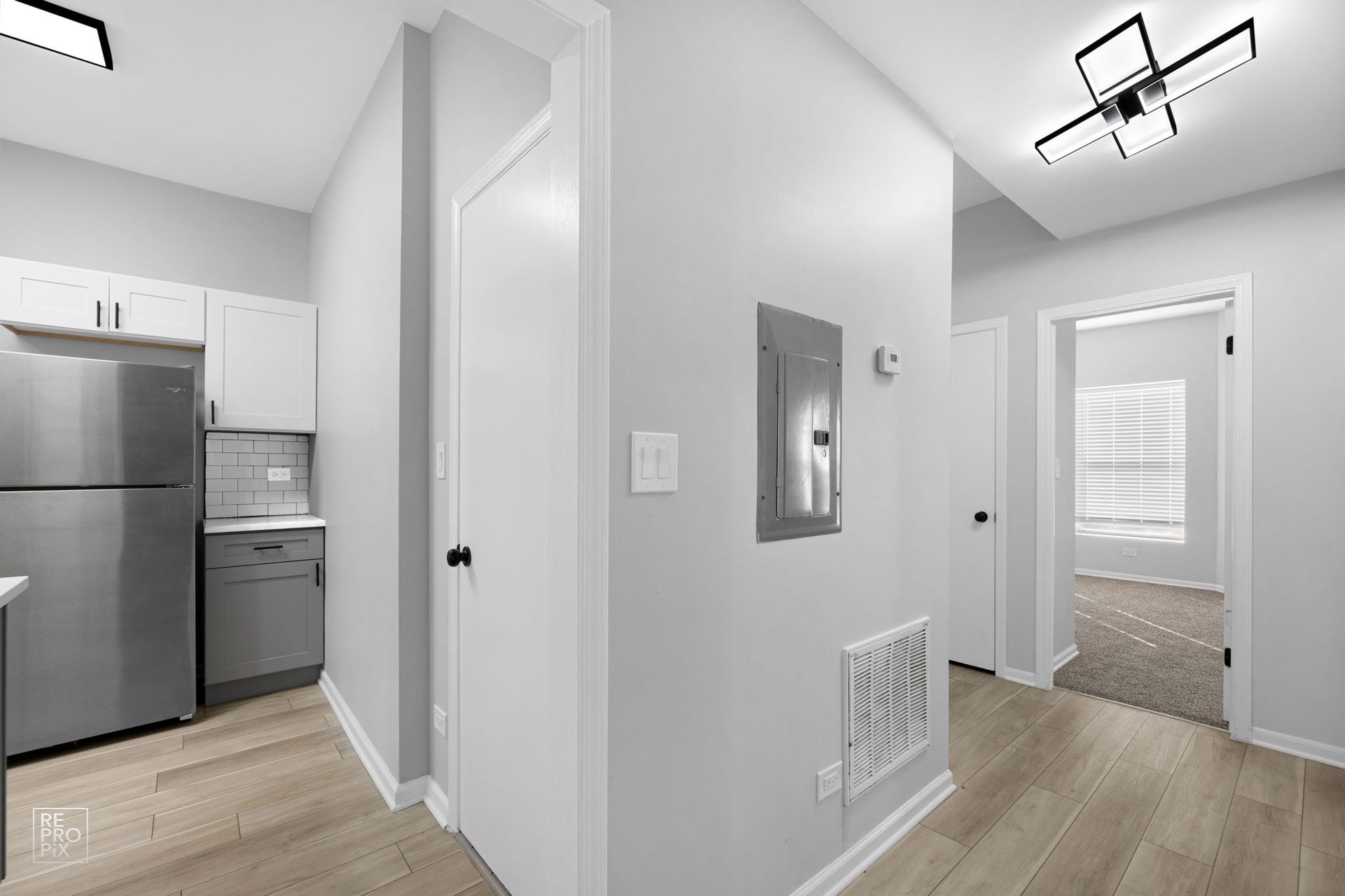 Hallway with kitchen visible, light gray walls, wooden floor, door, stainless steel refrigerator.
