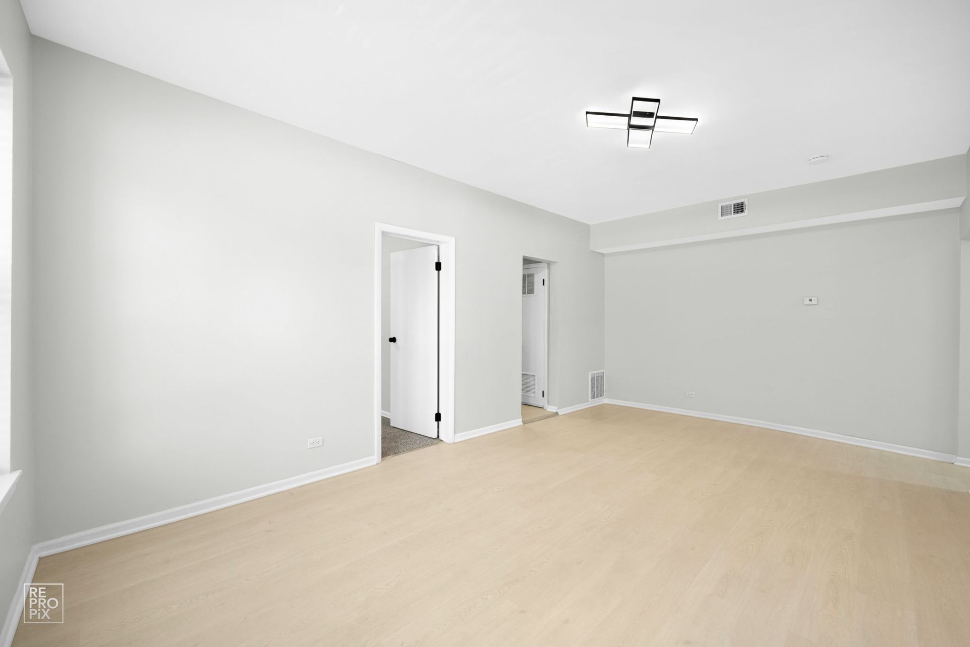 Empty room with light-colored walls and beige carpet. Two doorways and a window. Ceiling light fixture.