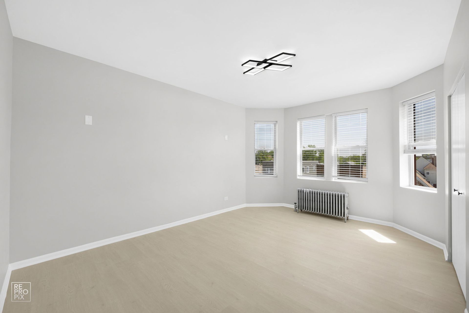 Empty room with light-colored flooring, grey walls, and windows. A radiator sits beneath the windows.