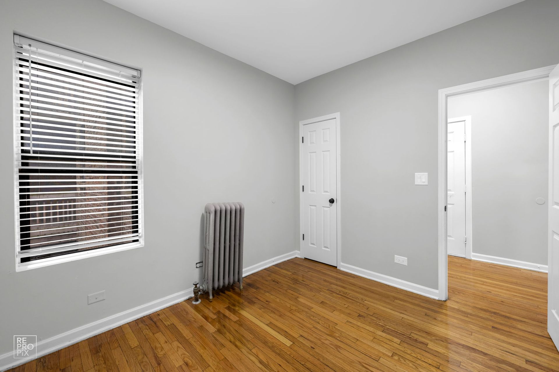 Empty room with hardwood floors, a window with blinds, and a radiator.