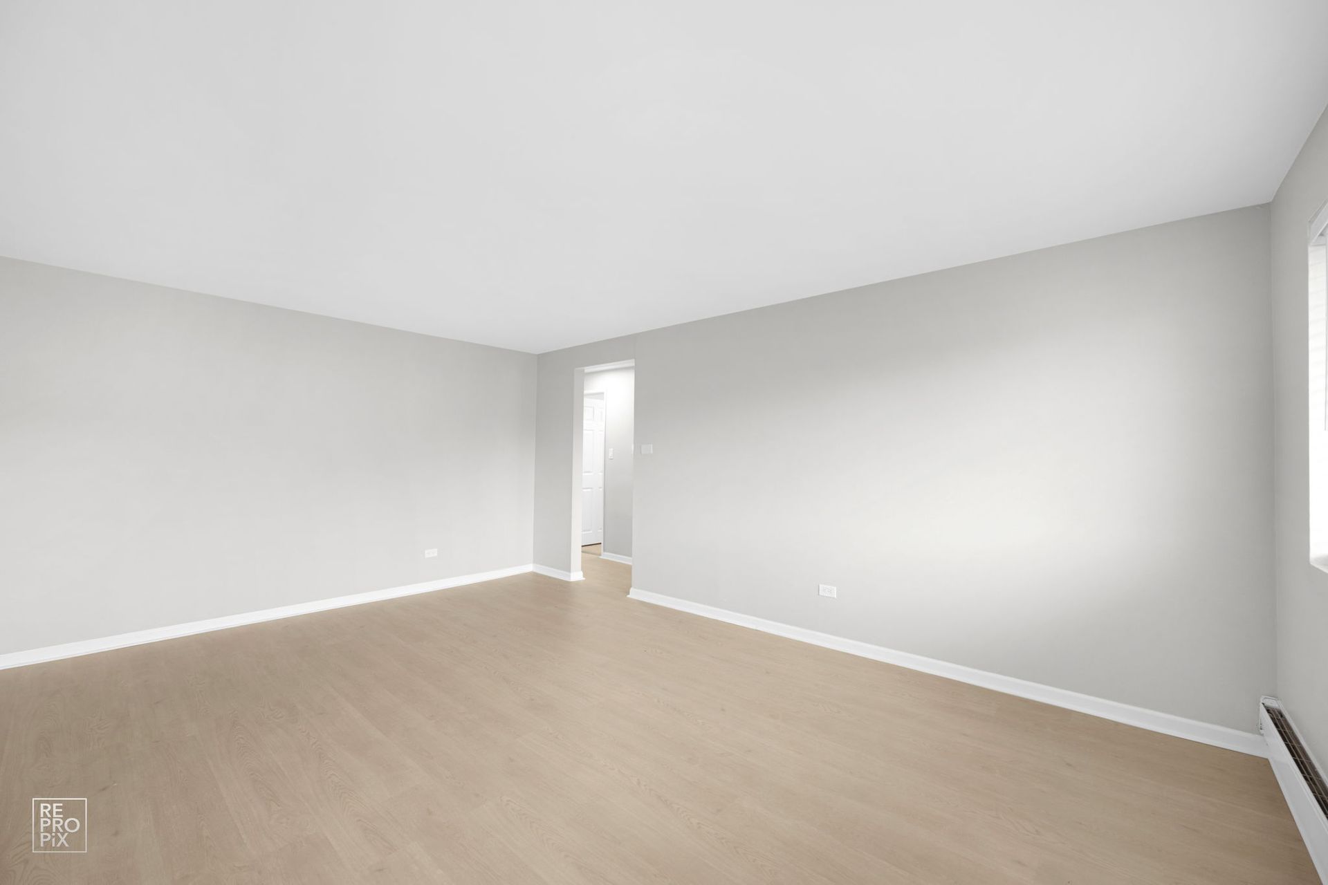 Empty room with pale walls, light wood flooring, and a doorway.
