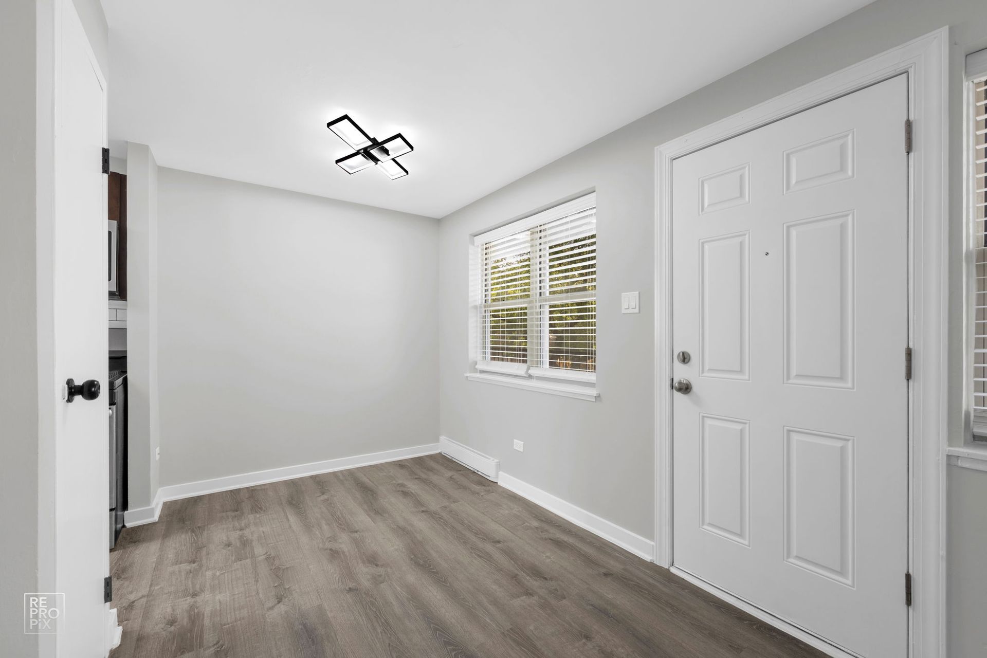 Empty, light-filled room with gray walls, wood-look floor, a white door and window with blinds.