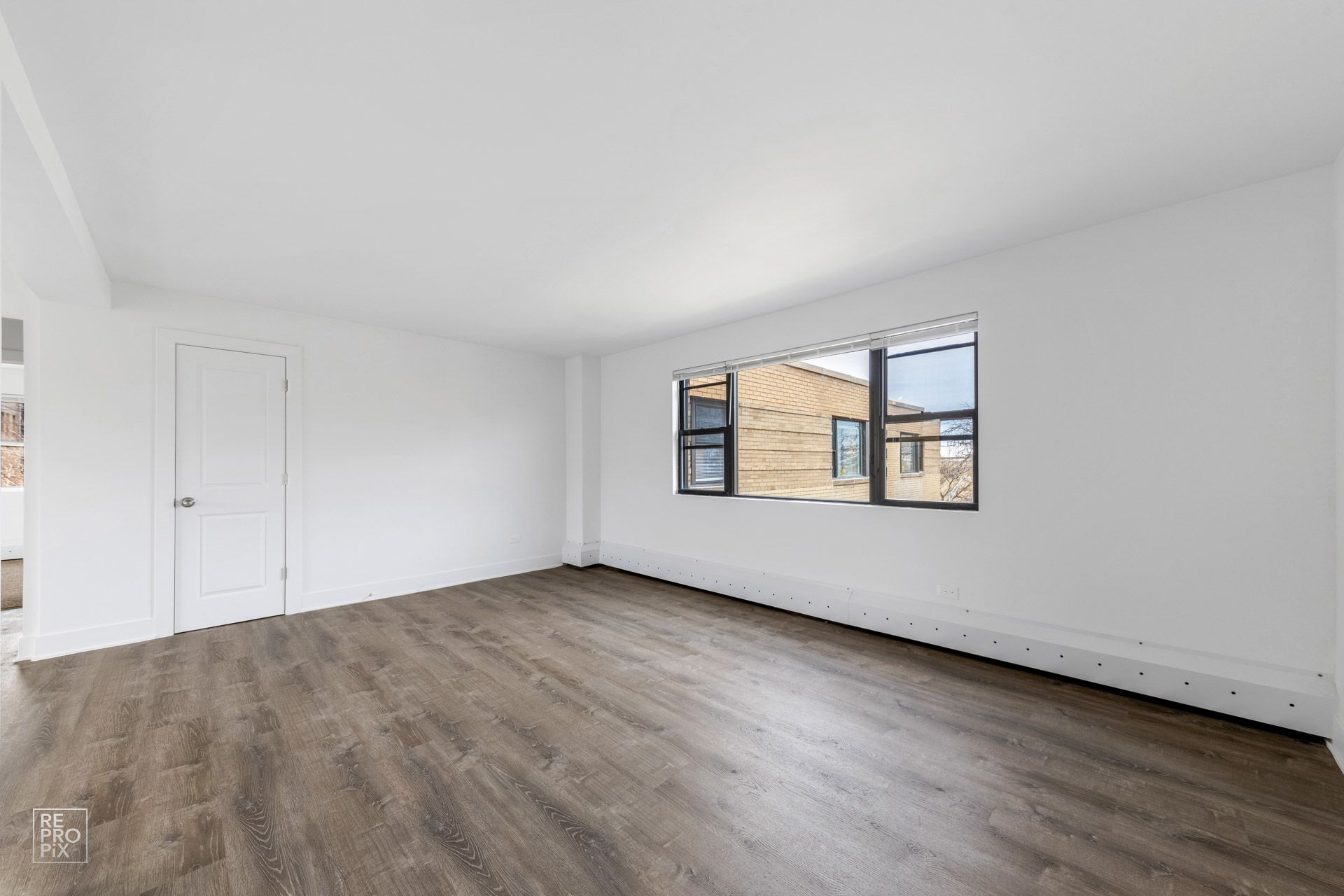 Empty room with wood-look flooring, white walls, a window, and a closed door.