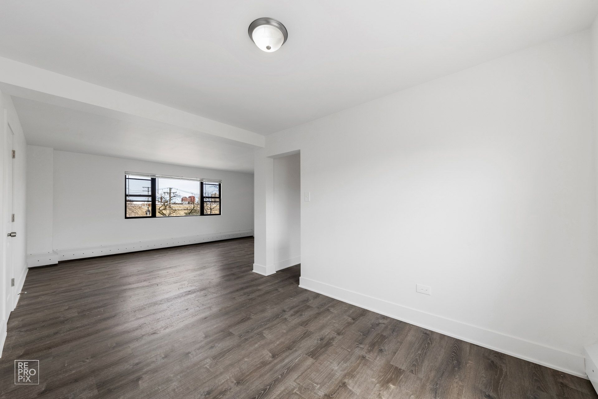 Empty room with white walls, dark wood-look flooring, and a window.