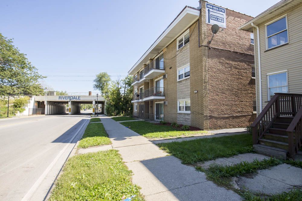 Apartment building next to a single-family home on a sunny street, near a road and underpass.