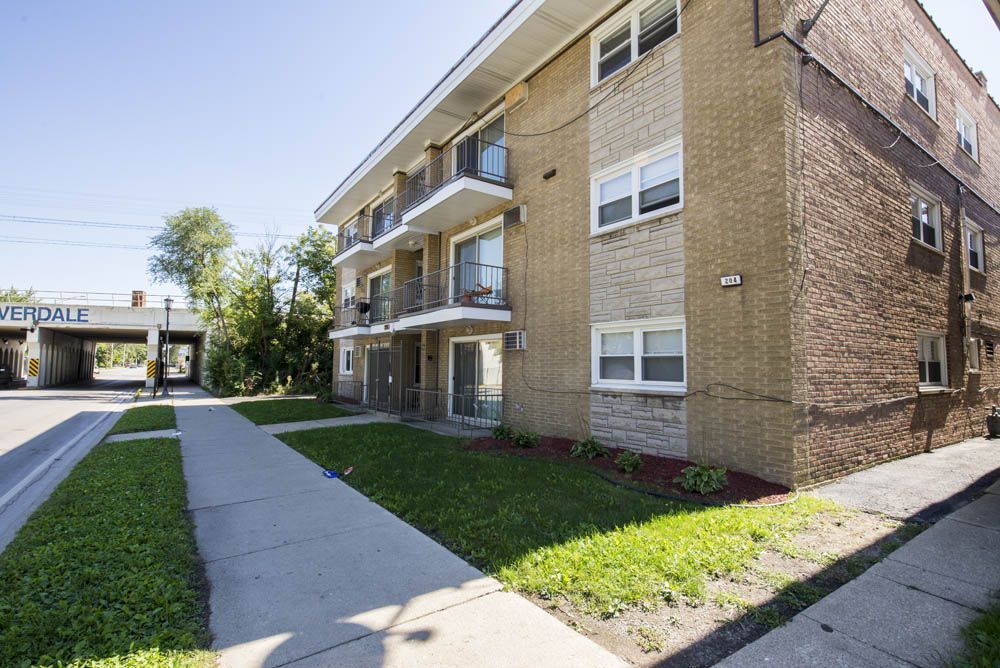 Apartment building with balconies and a walkway, next to a street and an overpass.