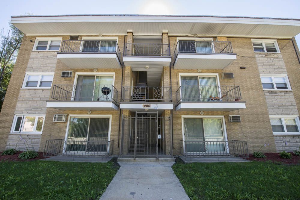 Three-story brick apartment building with balconies, metal gate, and walkway.