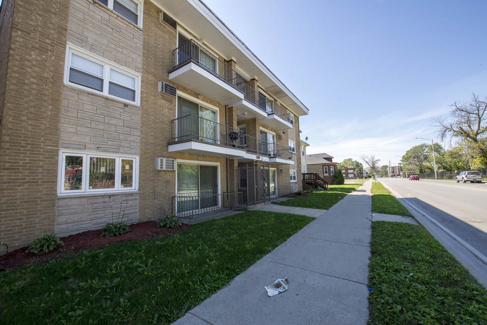 Apartment building with balconies and sidewalk next to a street with parked cars.