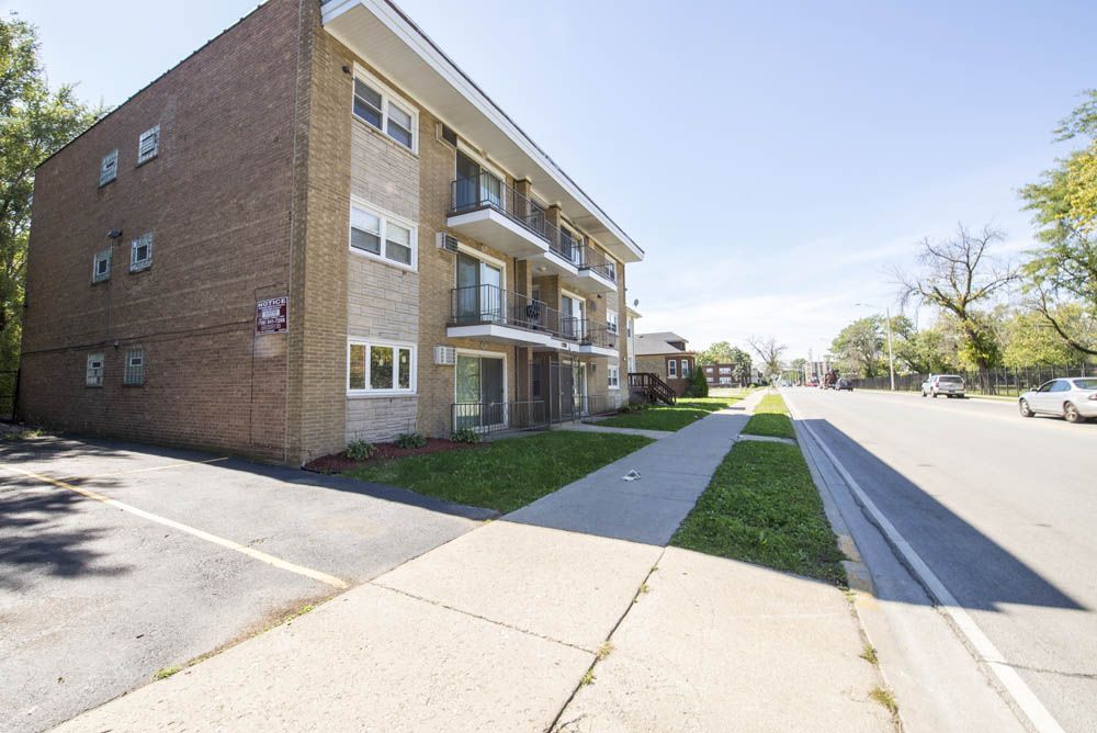 Brick apartment building with balconies, sidewalk, and street on a sunny day.
