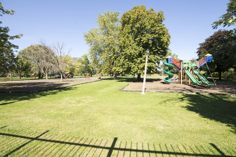 Park with playground equipment, trees, and a grassy area under a bright blue sky.