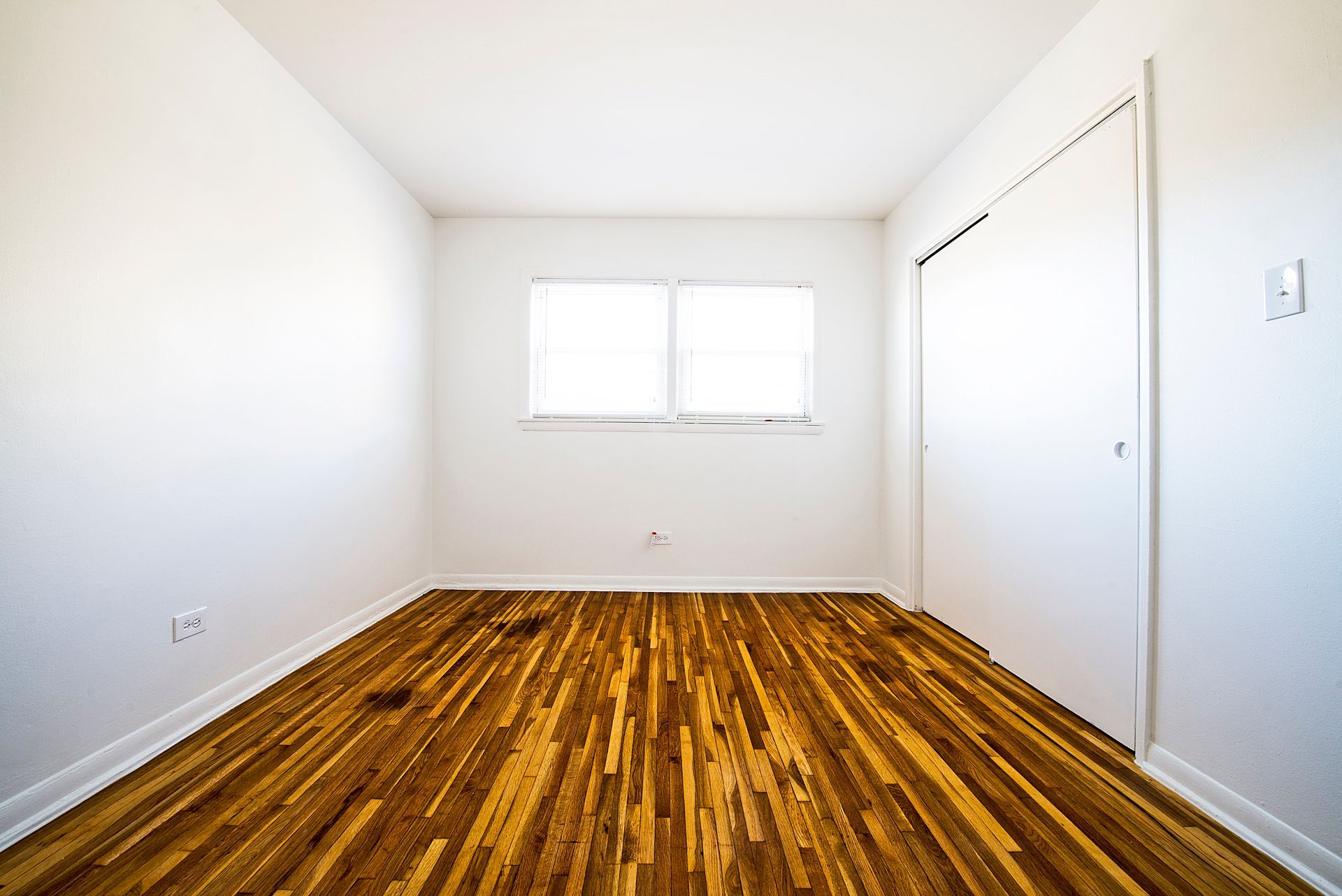 Empty room with wood floor, white walls, closet, and window.