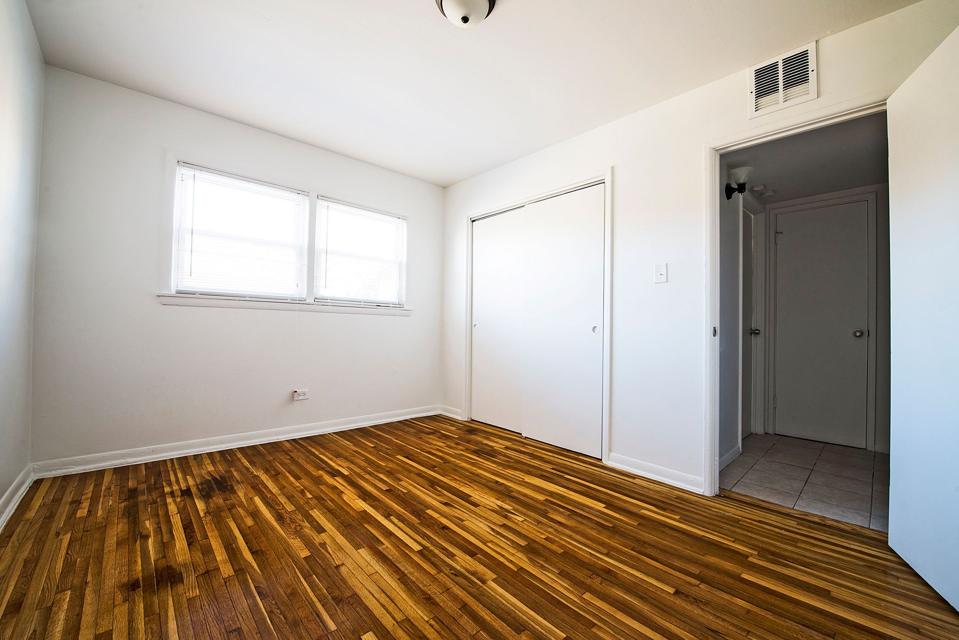 Empty bedroom with hardwood floors, a window, closet, and open doorway to a hallway.