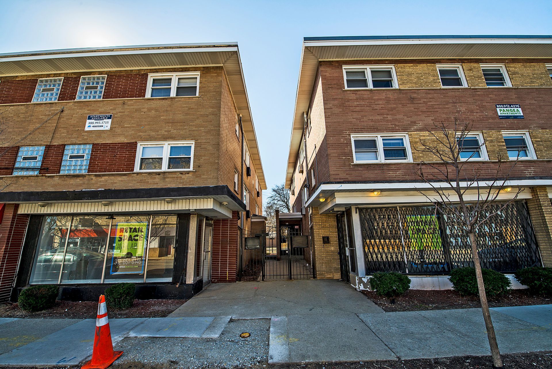 Two brick apartment buildings with storefronts on either side of a narrow walkway.