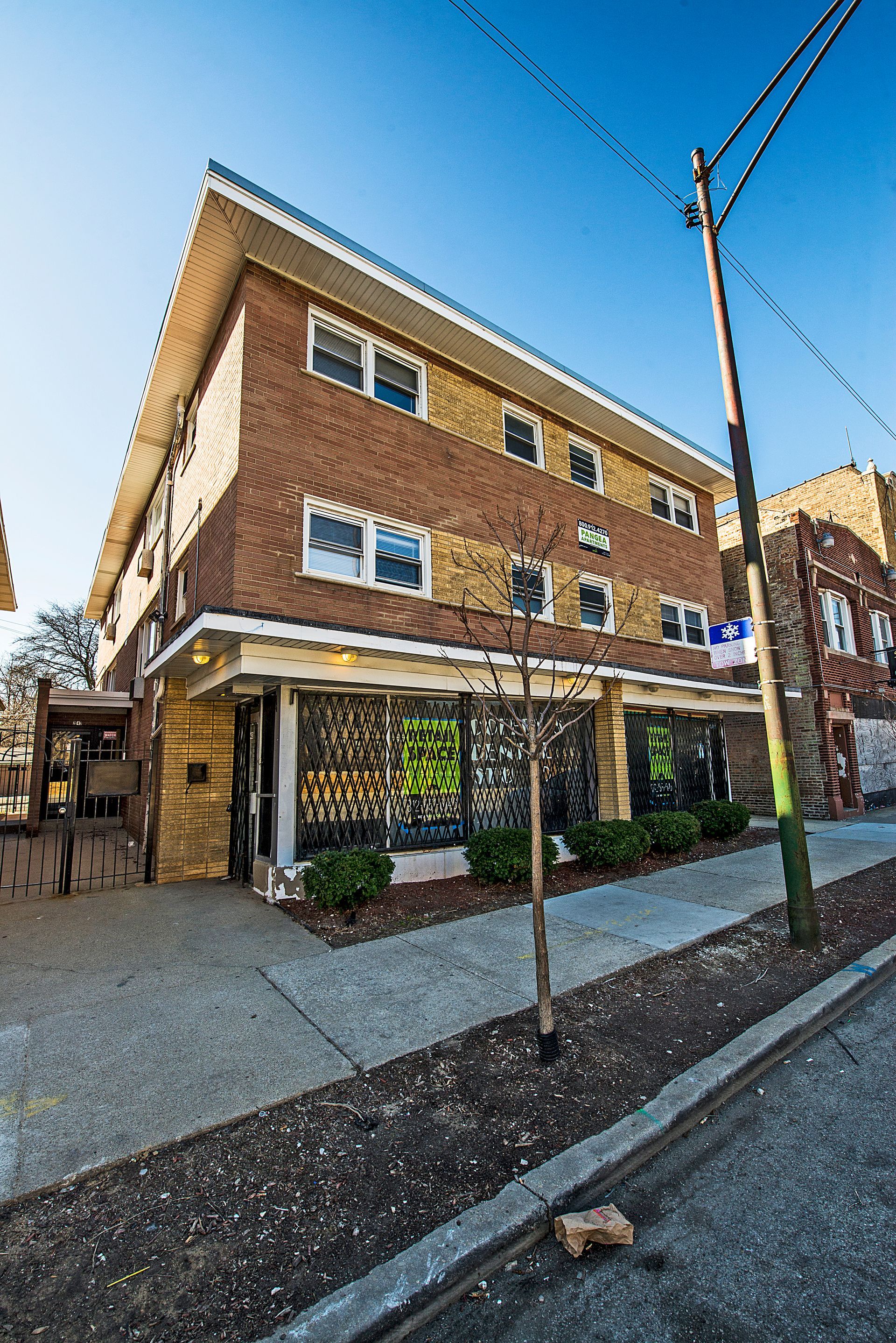 Brick building with storefronts on a sidewalk, a utility pole, and a sunny sky.