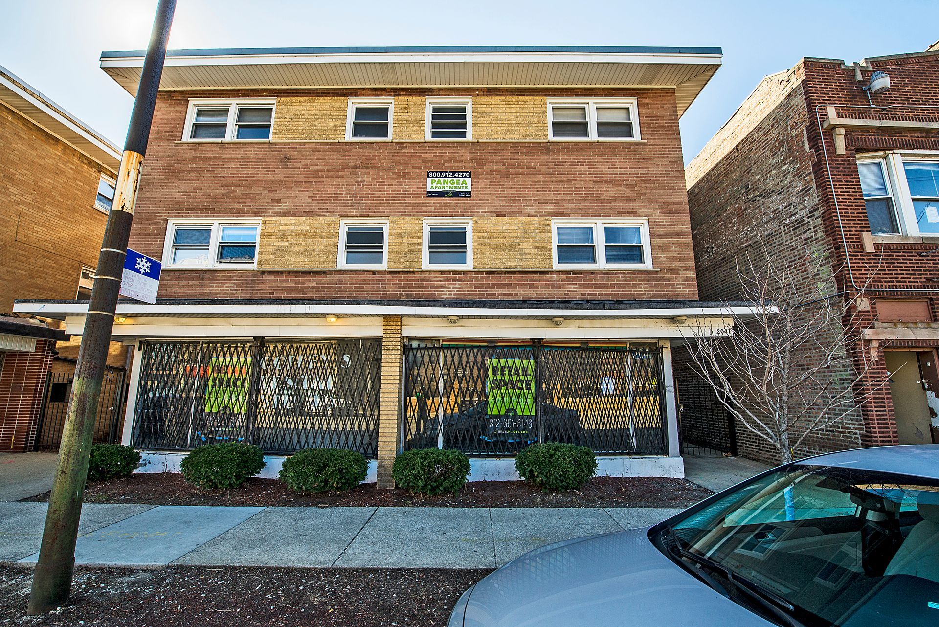 A two-story brick building with storefronts on the first floor, a car is parked in front.