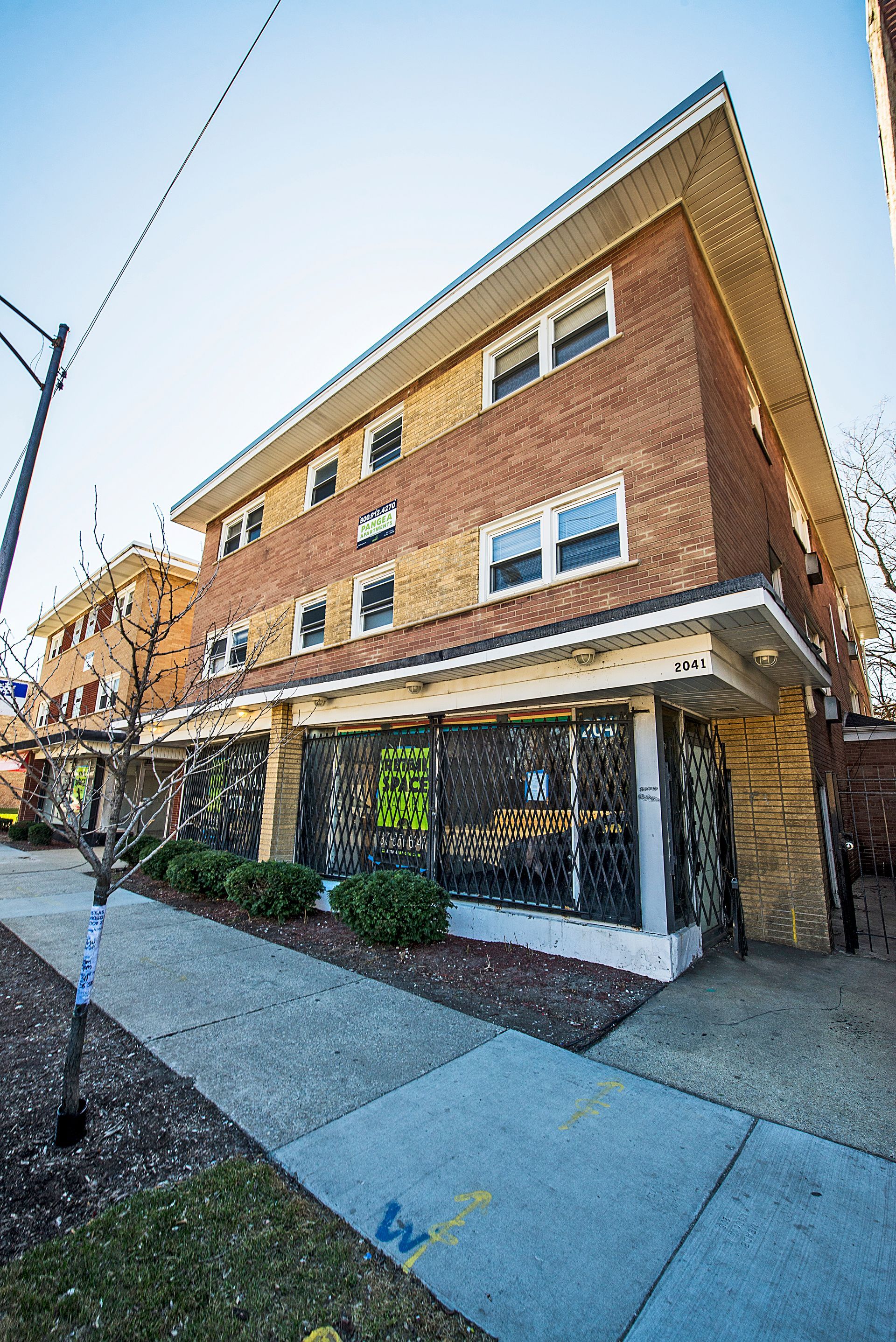 Brick apartment building with storefronts and sidewalk in daylight.