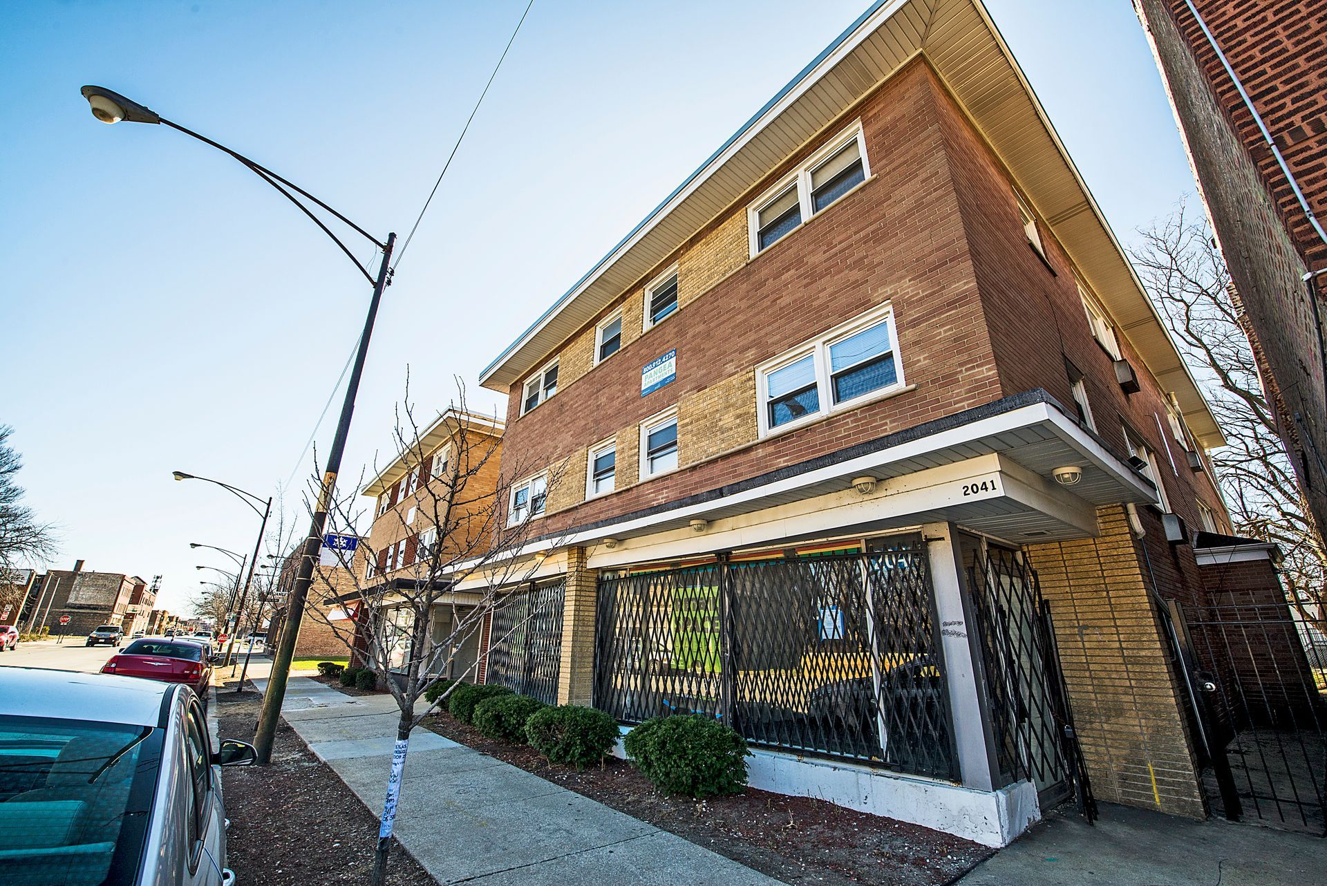 Brick building with three stories and barred storefronts on a city street.