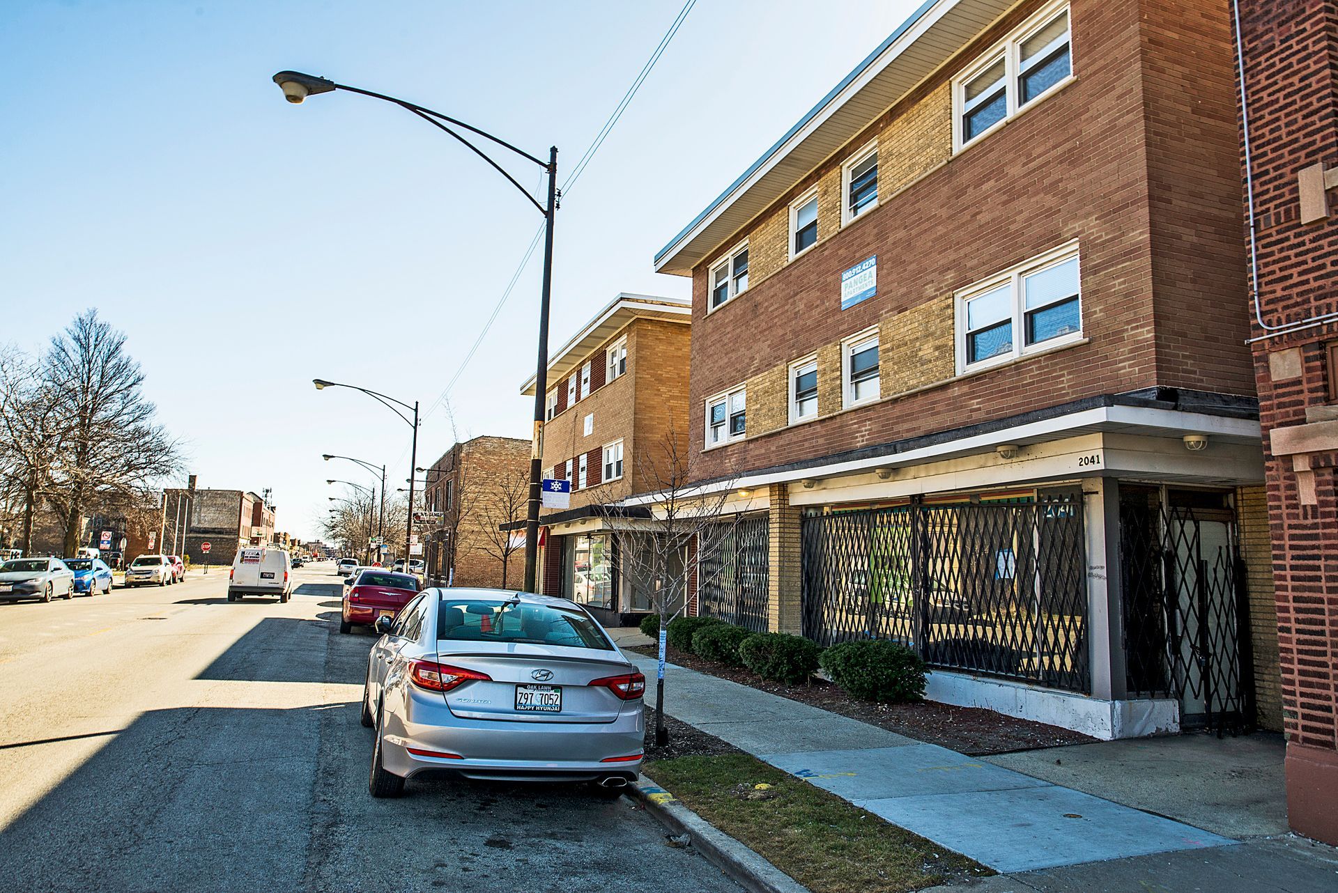 Street view of brick apartment buildings with cars parked on the side of the road.