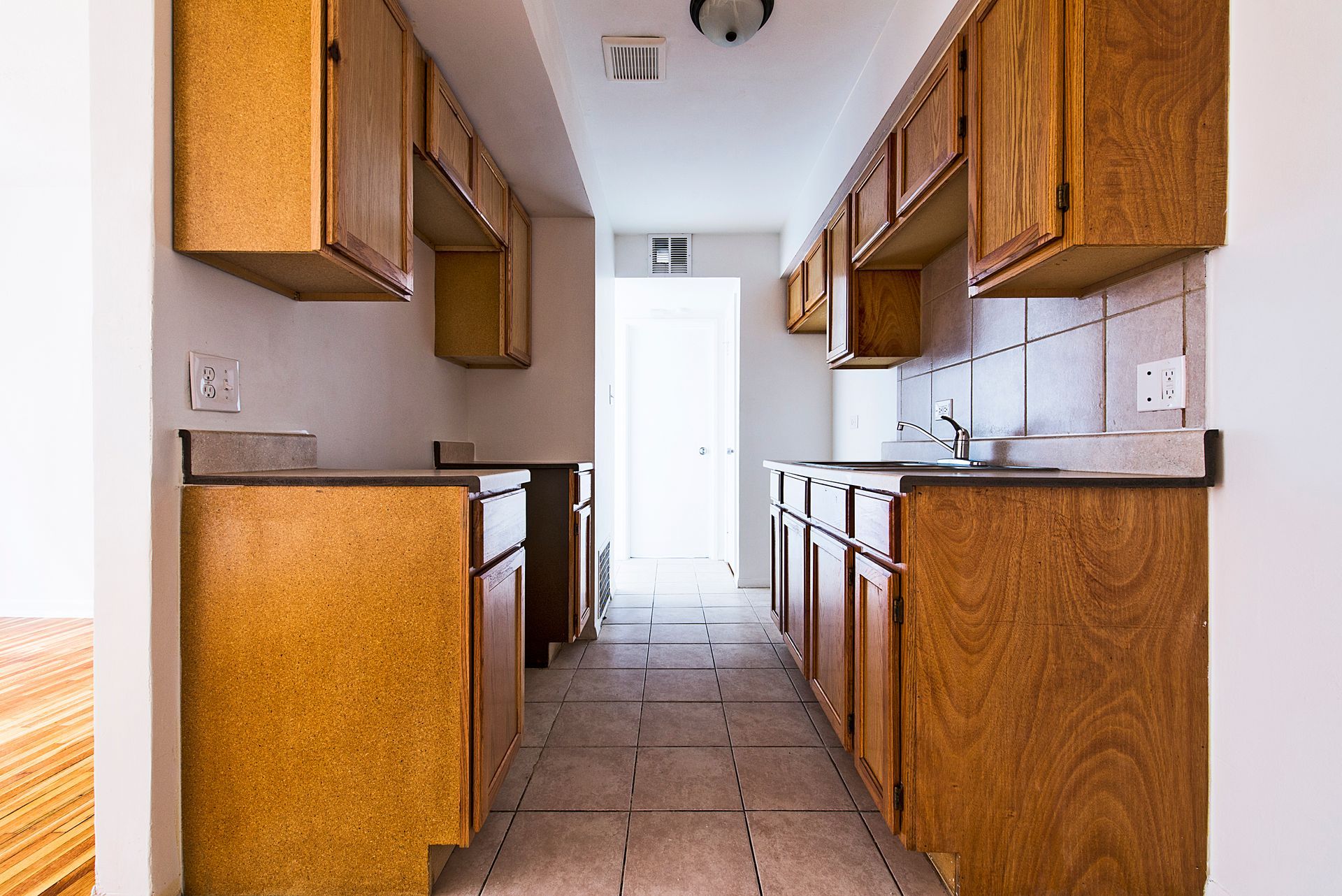 Narrow kitchen with wooden cabinets and countertops, bright natural light at the far end.