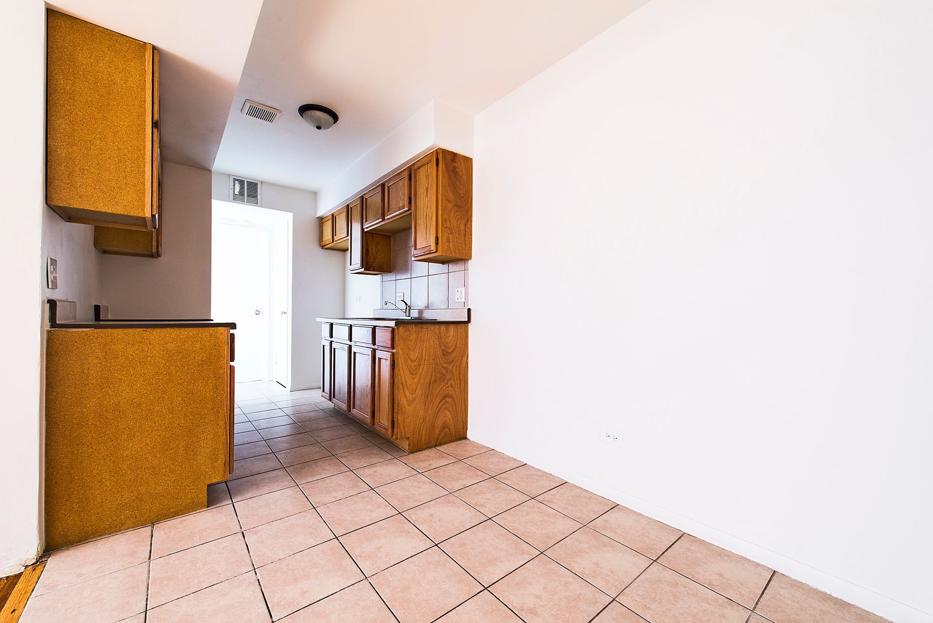Empty kitchen with light wood cabinets, white walls, and tiled floor.