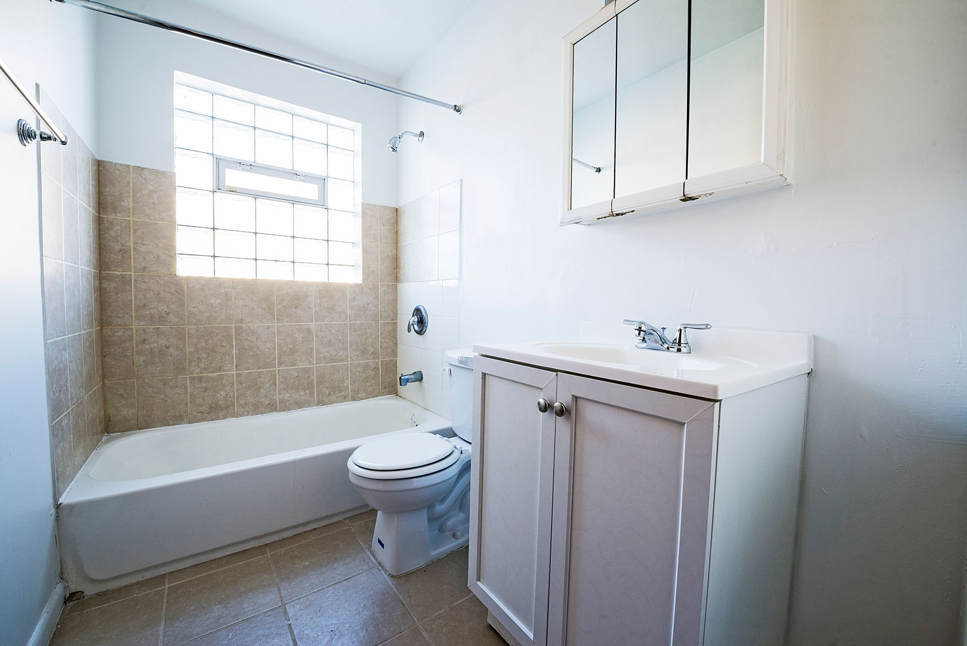 Bathroom with white walls, tan tile, tub, toilet, vanity, and mirrored cabinet.