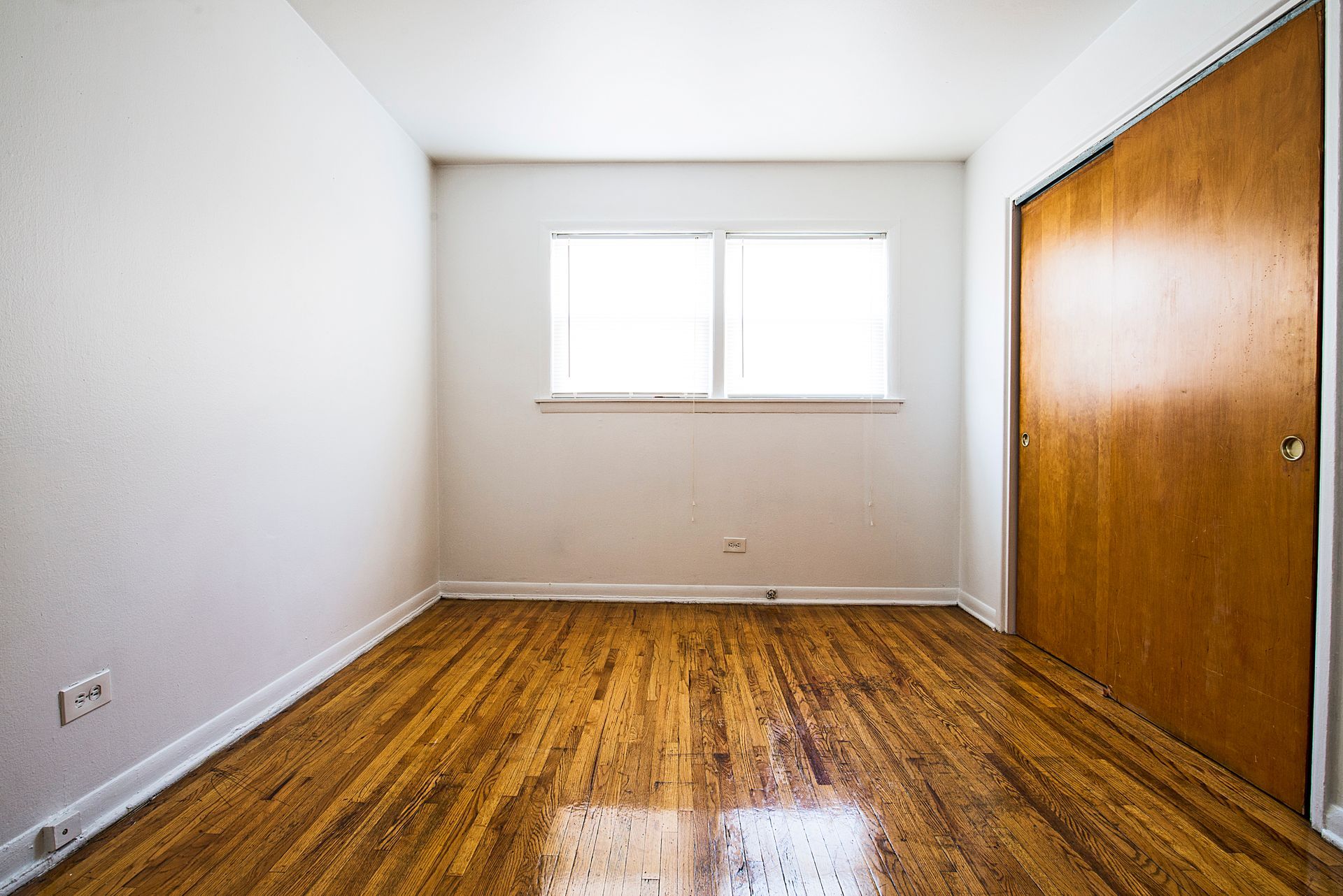 Empty room with wood floors, white walls, small window, and closet door.