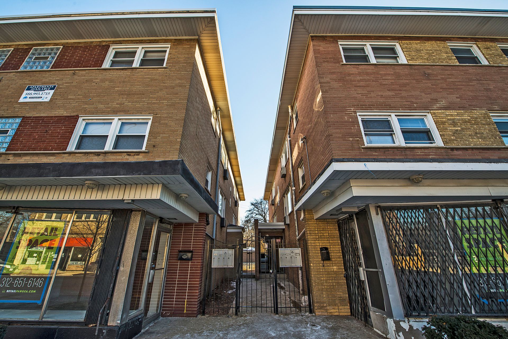 Two brick apartment buildings with retail spaces below, facing each other with an alleyway in between.